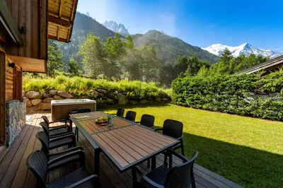 a wooden deck with a table and chairs on a lawn at Chalet Planards 2 in Chamonix-Mont-Blanc