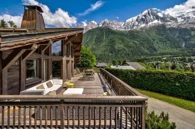 a house with a deck with mountains in the background at Chalet Le Favre in Chamonix-Mont-Blanc