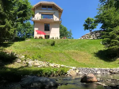 a house on top of a hill next to a river at Le Moulin des Olirics in Sallanches