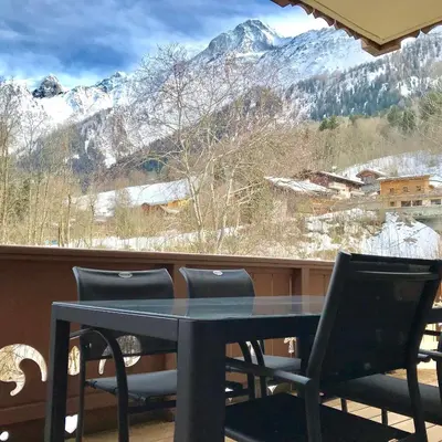 a table and chairs on a balcony with snow covered mountains at Kandahar in Les Houches