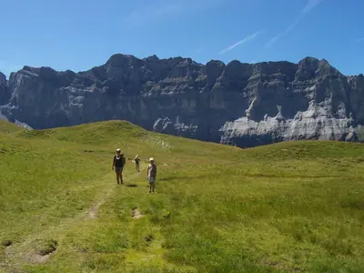 three people walking on a field with mountains in the background at Le Bivouac in Sixt