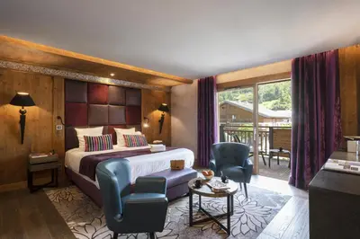 a hotel room with a bed and two chairs at MGM Hôtels & Résidences - Hôtel Les Suites d'Alexane in Samoëns