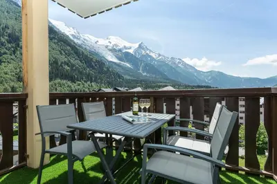 a table and chairs on a balcony with mountains at Apartment Aiglons - Central Chamonix Mountain Haven in Chamonix-Mont-Blanc