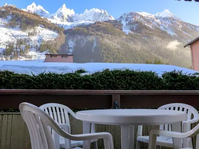 a table and chairs on a balcony with snow covered mountains at Apartment Ginabelle 1-1 by Interhome in Chamonix-Mont-Blanc