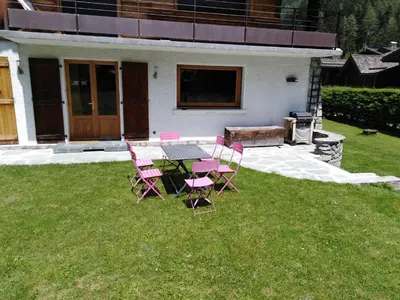 a patio with pink chairs and a table in the grass at Appartement avec Terrasse in Chamonix-Mont-Blanc