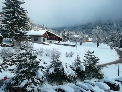a snow covered yard with cars parked in front of a house at Studio accueillant à Les Carroz, 27 m², vue montagne in Les Carroz d'Araches