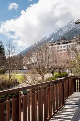a wooden bridge with a building and mountains in the background at APARTMENT PRESIDENT - Alpes Travel - Central Chamonix - Sleeps 12 in Chamonix-Mont-Blanc