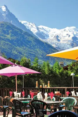 a patio with tables and chairs with mountains in the background at VTF Les Econtres in Chamonix-Mont-Blanc