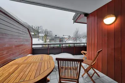 a wooden table and chairs on a balcony with snow at Carabiner: Residence Espace Montagne in Chamonix-Mont-Blanc