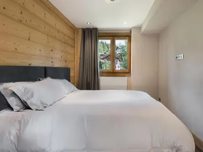 a bedroom with a large white bed with a wooden wall at Appartement rénové 2 chambres à Megève Centre avec balcon - FR-1-453-66 in Megève