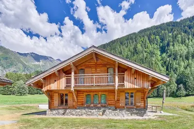 a log cabin in a field with mountains in the background at Chalet Coralie in Chamonix-Mont-Blanc