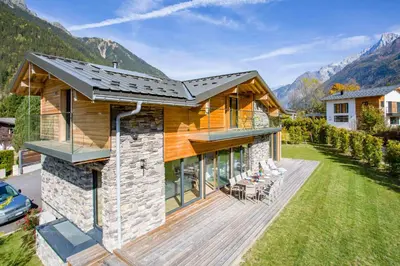 a house with a wooden deck and mountains in the background at Chalet Montana- Chamonix All Year in Chamonix-Mont-Blanc
