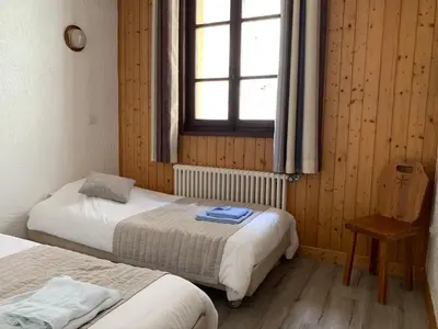 a bedroom with two beds and a window and a chair at Hotel des Lacs in Chamonix-Mont-Blanc