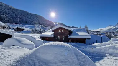 a house covered in snow with the sun behind it at Demi-Chalet Le Bief --Prox pistes in Les Carroz d'Araches