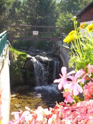a bridge over a waterfall with pink flowers at Appartement L'Ecureuil 8 pers -Prox pistes et centre village- in Les Carroz d'Araches