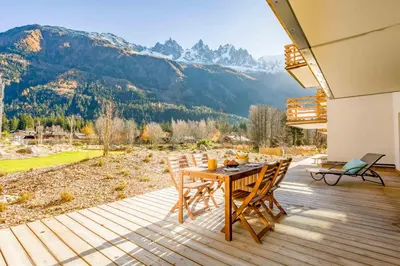 a wooden deck with a table and chairs and mountains at La Cordee 504 Apartment - Chamonix All Year in Chamonix-Mont-Blanc