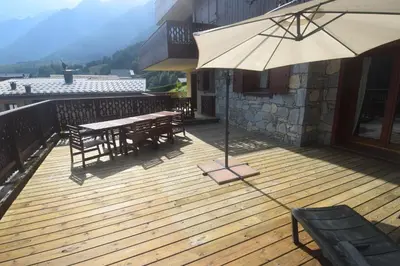 a wooden deck with a table and chairs and an umbrella at Spacious Apartment 2 Minutes from Ski Lift, Equipped for Babies in Les Houches