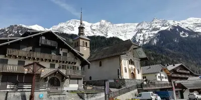a building with a church with mountains in the background at Le Lièvre Blanc, appartement N°2 in Les Contamines-Montjoie
