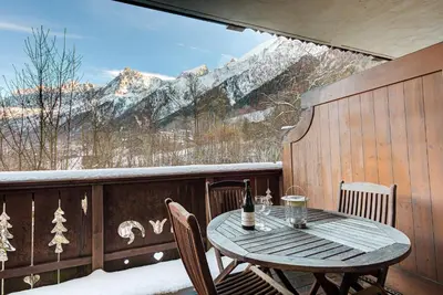 a table and chairs on a balcony with snow covered mountains at APARTMENT KANDAHAR - Alpes Travel - Central Chamonix - Sleeps 4 in Les Houches