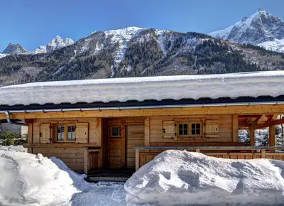 a log cabin in the snow with mountains in the background at Chalets Ile des Barrats in Chamonix-Mont-Blanc