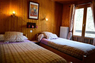 two beds in a room with wooden walls and a window at Crêmerie Balmat in Chamonix-Mont-Blanc