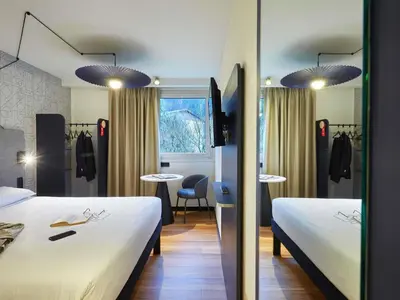 a hotel room with two beds and a table at Ibis Sallanches Porte du MontBlanc in Sallanches