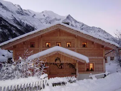 a log cabin covered in snow with mountains in the background at Chalet Altitude 1057 in Chamonix-Mont-Blanc