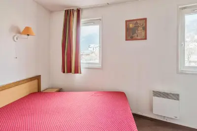 a bedroom with a pink bed and two windows at maeva Home Résidence la Rivière in Chamonix-Mont-Blanc