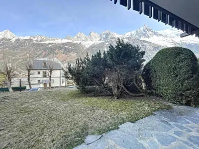 a house with trees and snow capped mountains in the background at Appartement Chaleureux à Chamonix, 4 Pers, Près du Brévent avec Terrasse et Parking - FR-1-507-26 in Chamonix-Mont-Blanc