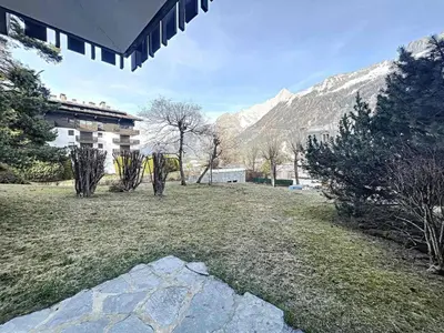 a yard with a building and mountains in the background at Appartement Chaleureux à Chamonix, 4 Pers, Près du Brévent avec Terrasse et Parking - FR-1-507-26 in Chamonix-Mont-Blanc