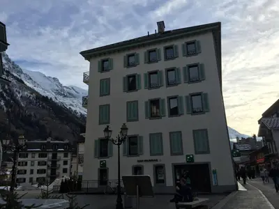 a large white building with green windows and a mountain at Appartement cosy au centre de Chamonix avec jardin, 2 pièces, bien équipé, accepte animaux - FR-1-507-29 in Chamonix-Mont-Blanc