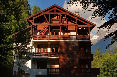 a large wooden building with a balcony and mountains at Les Campanules in Les Houches
