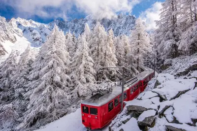 a red train traveling through the snow covered mountains at Chalet CLADIE - Private Jacuzzi & Sauna - View of Mont Blanc range - By Cozee Rentals in Les Houches
