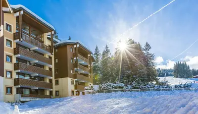 a building in the snow with the sun behind it at Résidence Odalys Le Buet in Morillon