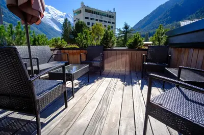 a deck with chairs and tables and a snow covered mountain at Maison Des Praz Chamonix in Chamonix-Mont-Blanc