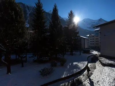 a snow covered yard with trees and a building and the sun at Studio Chamonix 20m², 4 pers, balcon, parking - FR-1-517-40 in Chamonix-Mont-Blanc