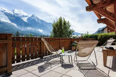 two chairs and a table on a balcony with mountains at Chalet La Chaumière in Chamonix-Mont-Blanc