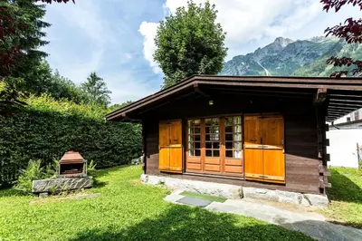 a small cabin in the grass with mountains in the background at Mazot Loppe - A Cosy Central Chamonix Hideaway in Chamonix-Mont-Blanc