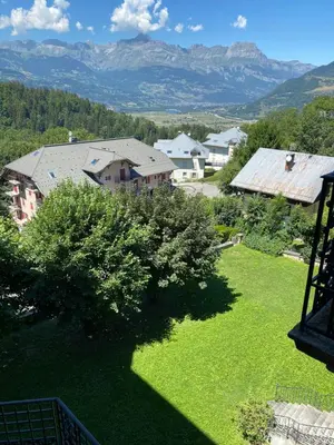 a green yard with a house and mountains in the background at Mont Blanc Residence in Saint-Gervais-les-Bains