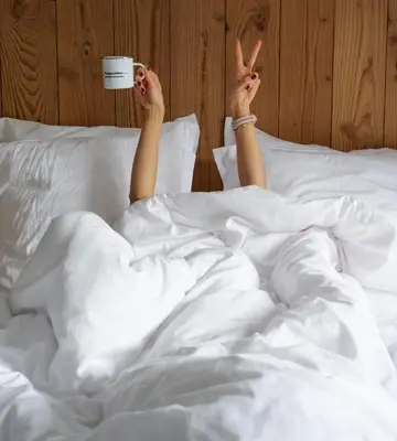 a woman laying in bed with a cup of coffee at PlanB Hotel - Living Chamonix in Chamonix-Mont-Blanc