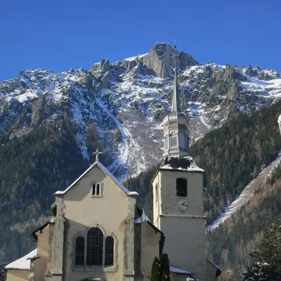 a church with a clock tower in front of a mountain at Hotel Le Chamonix in Chamonix-Mont-Blanc