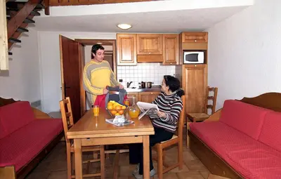 a man and a woman sitting at a table in a kitchen at Résidence Odalys Le Front de Neige in Les Carroz d'Araches