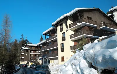 a snow covered building with cars parked in front of it at Résidence Odalys Le Front de Neige in Les Carroz d'Araches