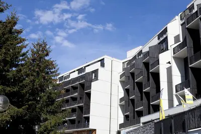 a white building with black windows and a tree at Residence La Foret - maeva Home in Arâches-la-Frasse