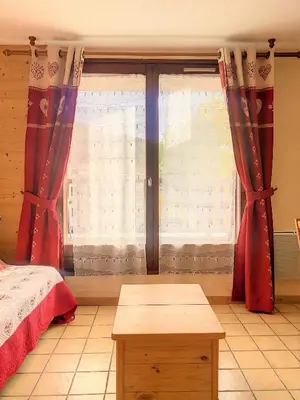 a bedroom with a bed and a window with red curtains at SH104 - Studio 4 pers centre des Carroz in Les Carroz d'Araches