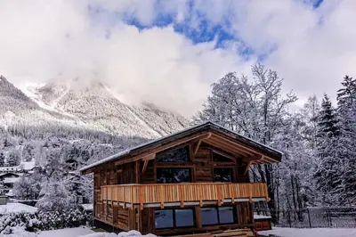 a log cabin with snow covered mountains in the background at Chalet des Amis appt 1 - Chamonix All Year in Chamonix-Mont-Blanc