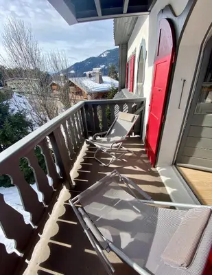 a table and chairs on a balcony with a red door at Appartement Odyssée - Welkeys in Megève