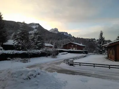 a road covered in snow with a mountain in the background at Le chalet des neiges 2 est au calme situé à 5 mn à pied du centre il est composé d'1 chambre avec lit double plus canapé convertible parking privé sur place et arrêt navette gratuite à 30 m in Les Carroz d'Araches