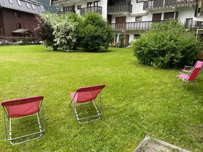 three chairs sitting in the grass in front of a building at Appartement style chalet avec grande terrasse et parking prive in Chamonix-Mont-Blanc