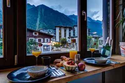 a table with food and drinks and a window with a view at Chamonix City Center Luxury Studio Apartment in Chamonix-Mont-Blanc